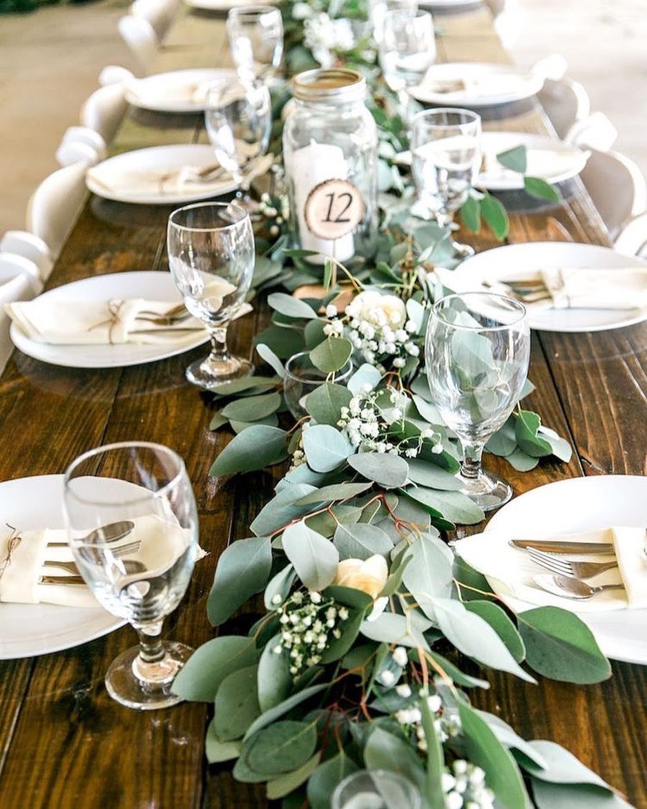 Eucalyptus and white flower greenery runner decorating a long wooden wedding reception table.