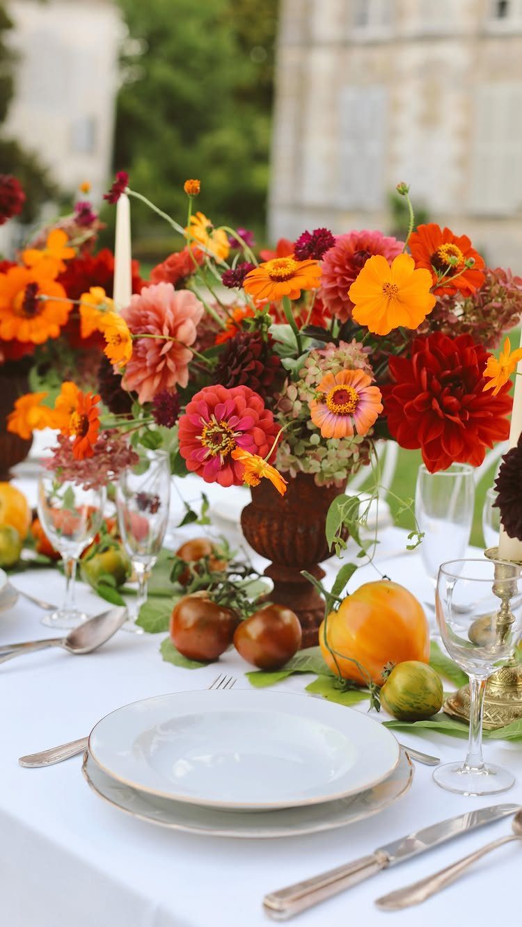 Large, colorful floral centerpiece with zinnias and dahlias in a wooden vase on a white table.