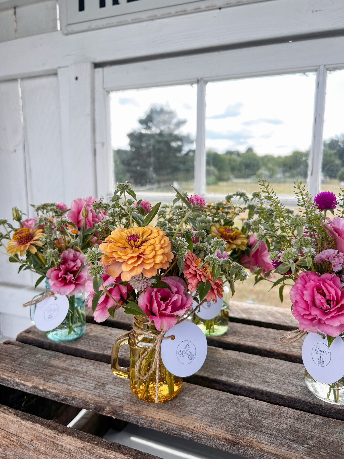 Colorful wildflowers in small mason jars arranged on a rustic wooden table.
