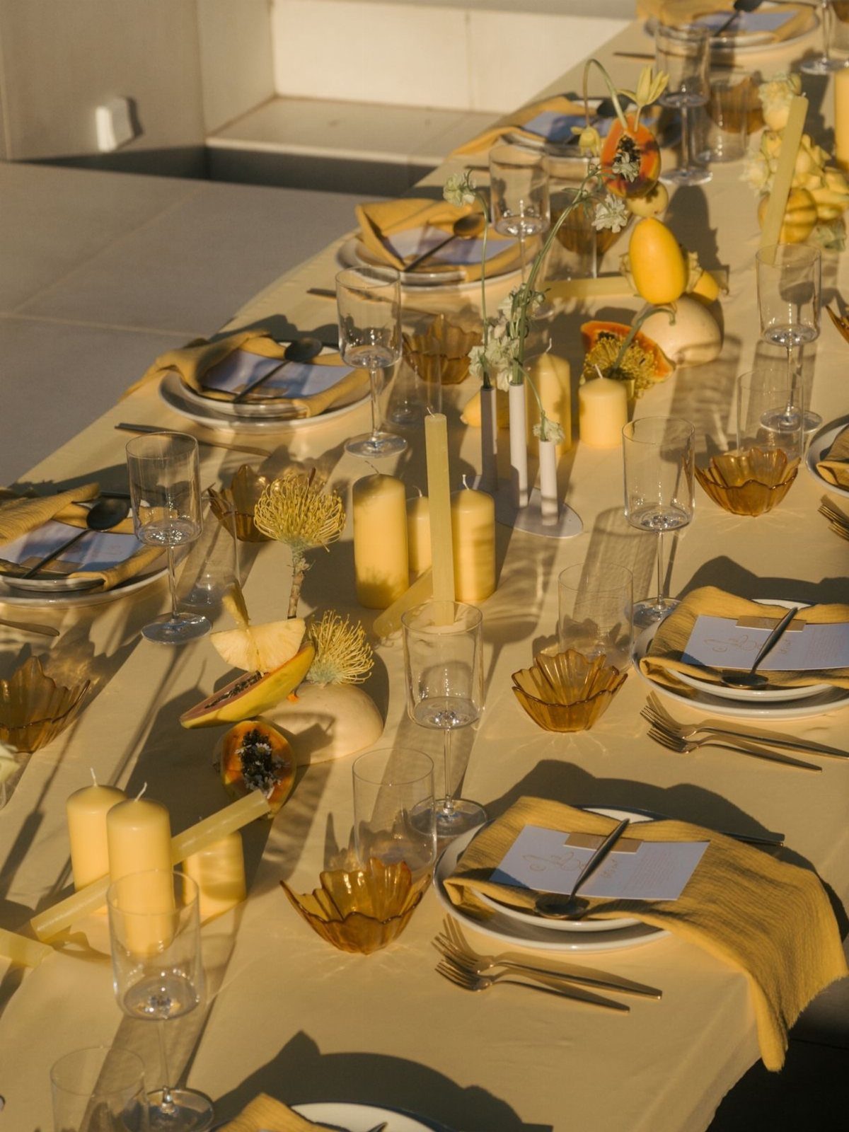 A long dining table decorated with yellow pillar candles, white flowers, and gold accents.