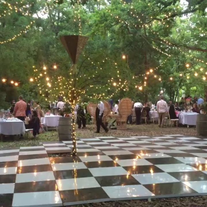 12 Forest Wedding Reception Ideas Under Lanterns and Light 10 A checkered dance floor under string lights in a wooded outdoor wedding reception area.