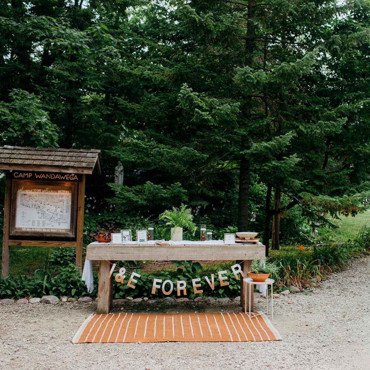 12 Forest Wedding Reception Ideas Under Lanterns and Light 12 A decorated wooden table with a celebratory banner set against a lush forest background.