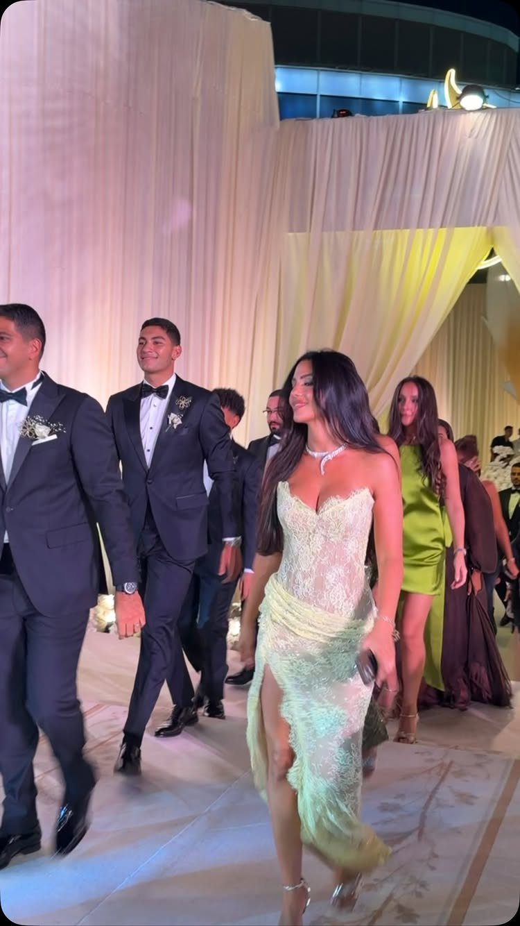 A woman wearing a light green strapless lace evening gown walking through a formal event.