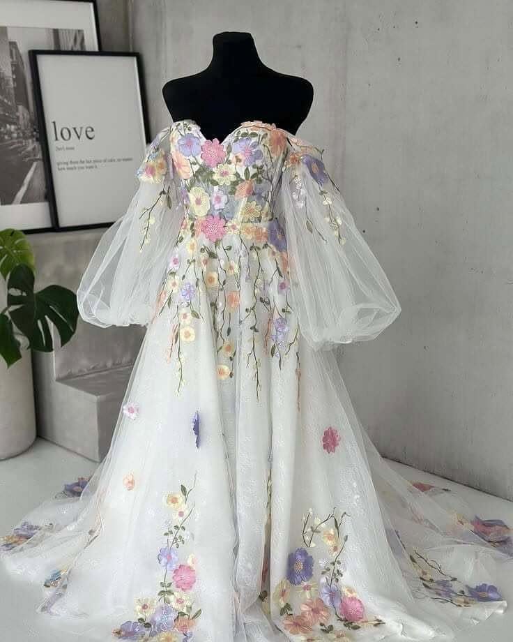 A white wedding dress with colorful floral embroidery and large sheer puff sleeves on a mannequin.