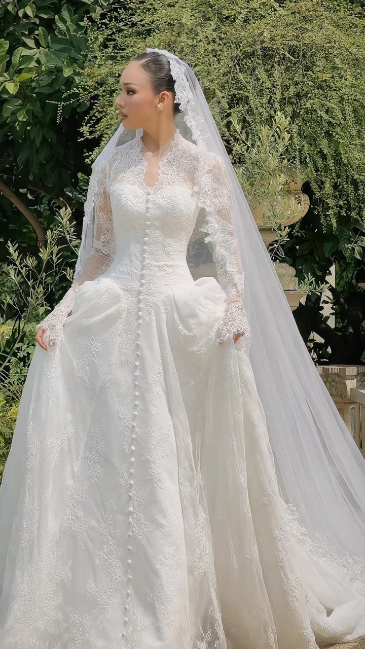 Woman wearing a long-sleeved lace wedding dress and a sheer veil in a garden.