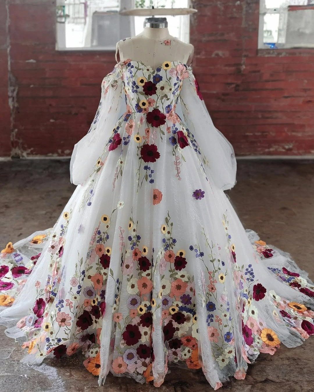 An ivory wedding dress with colorful floral appliqués displayed on a mannequin.