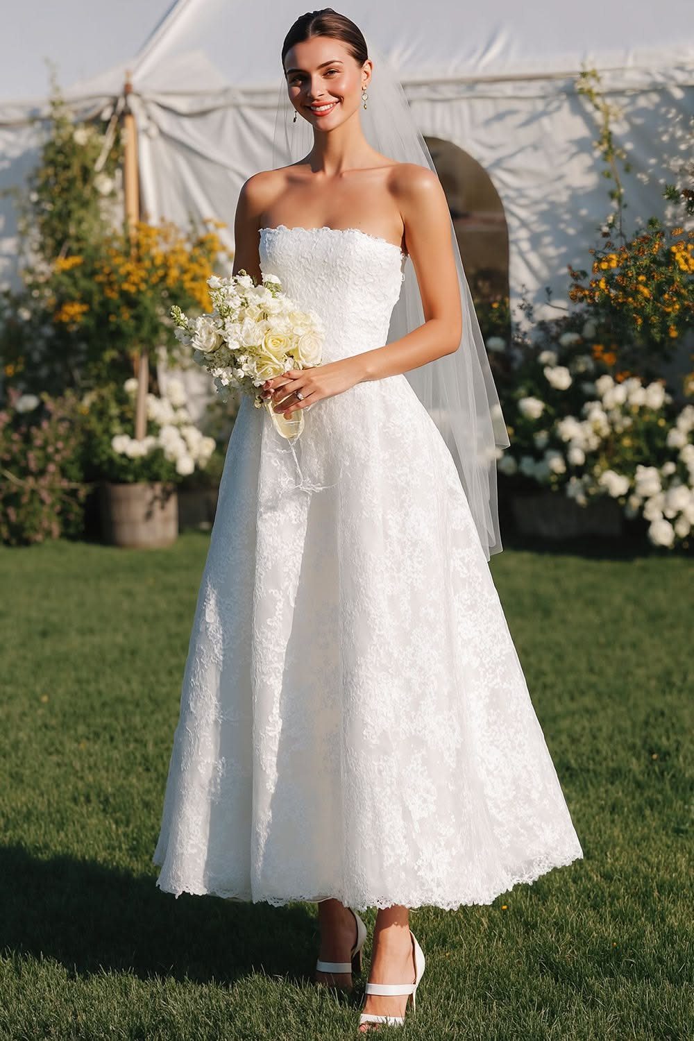 A woman in a white strapless lace wedding dress holding a bouquet in a garden setting.