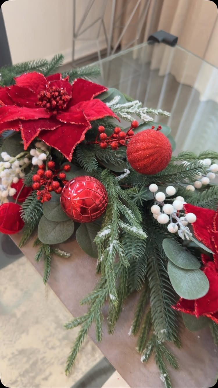 Christmas garland with red poinsettias, red ornaments, and greenery resting on a glass table surface.