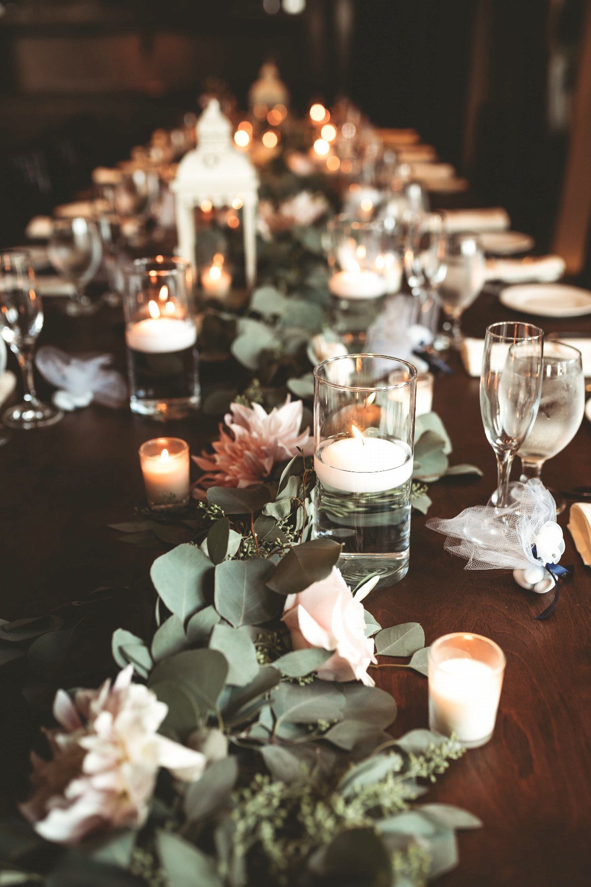 Eucalyptus leaves and pink flowers arranged in a garland on a dark wooden dining table.