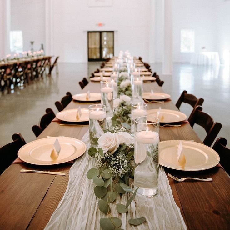 Greenery garland with white roses and floating candles in glass cylinders on a long wooden table.