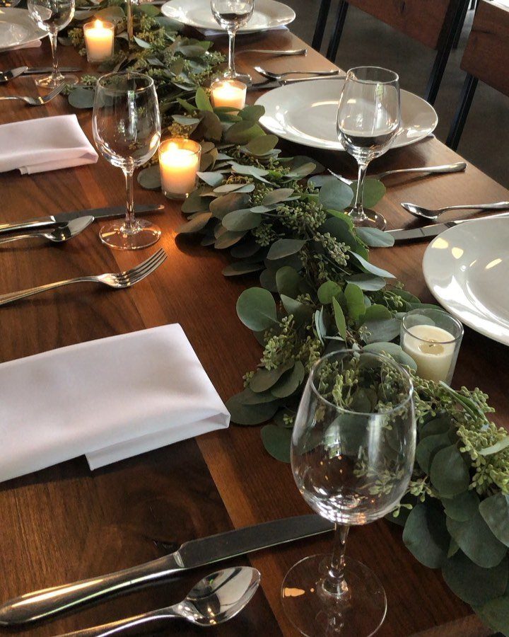 Eucalyptus greenery garland with small white candles running down the center of a wooden dining table.