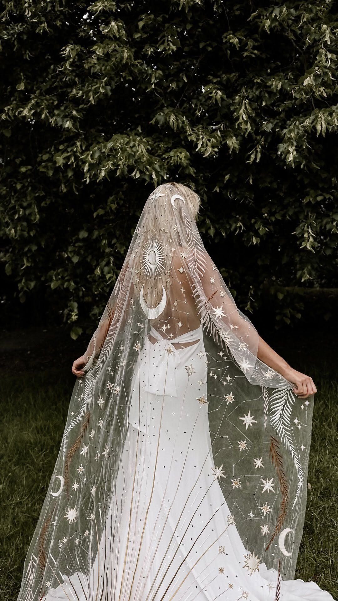Woman wearing a white wedding dress with a celestial motif sheer veil outdoors.
