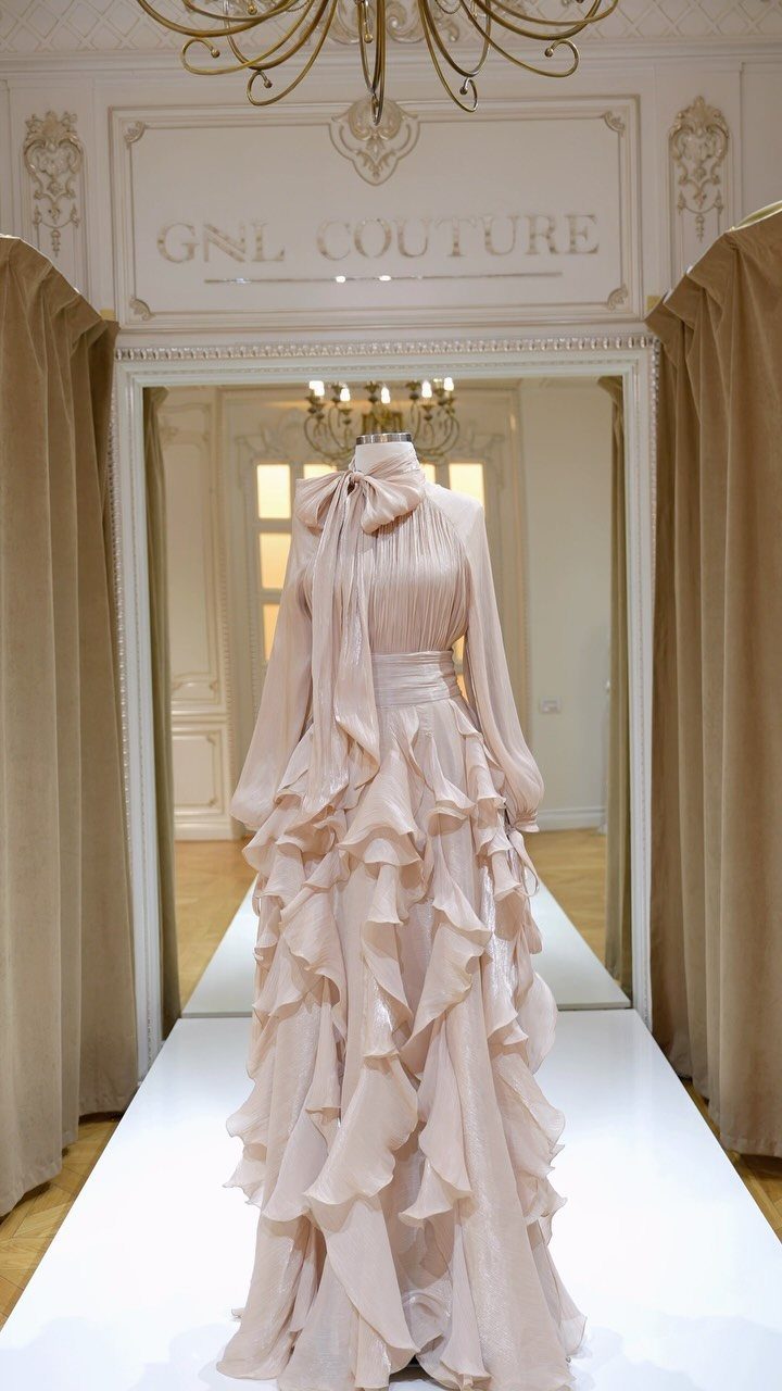 A pale pink chiffon maxi dress with a large bow neck and ruffled skirt on a mannequin.