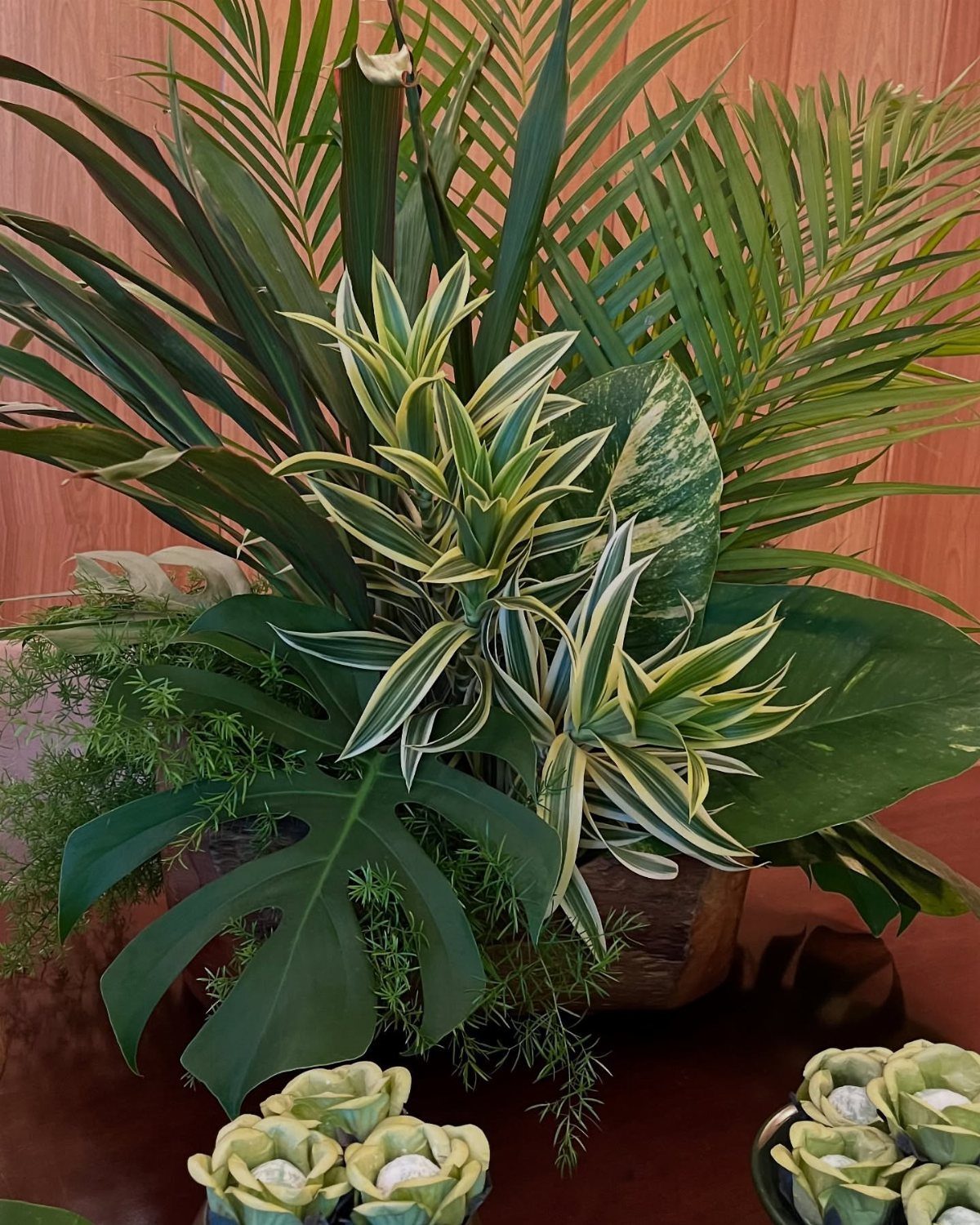 Tropical green leaves in a wooden planter with small artichoke-style tea light candles on a table.