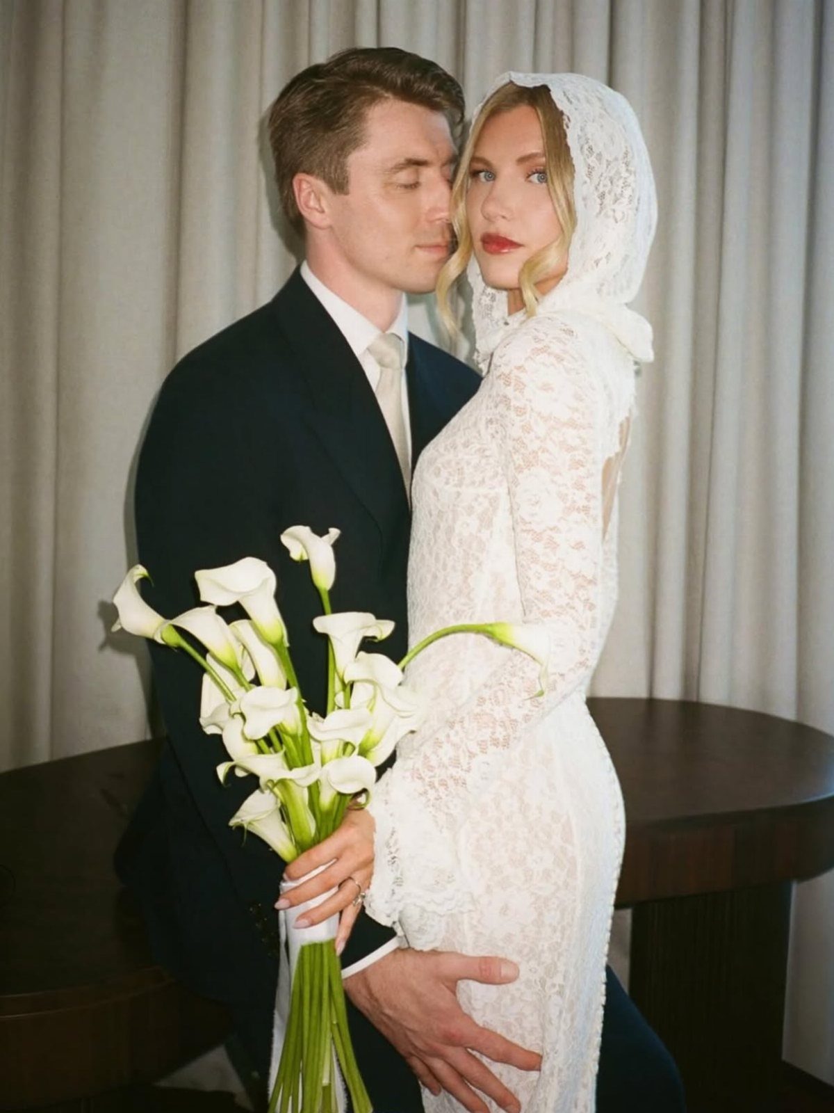 Hooded Wedding Dress: 6 Ideas from Vintage to Modern 6 A woman wearing a white lace hooded wedding dress holding calla lilies while posing with a man.