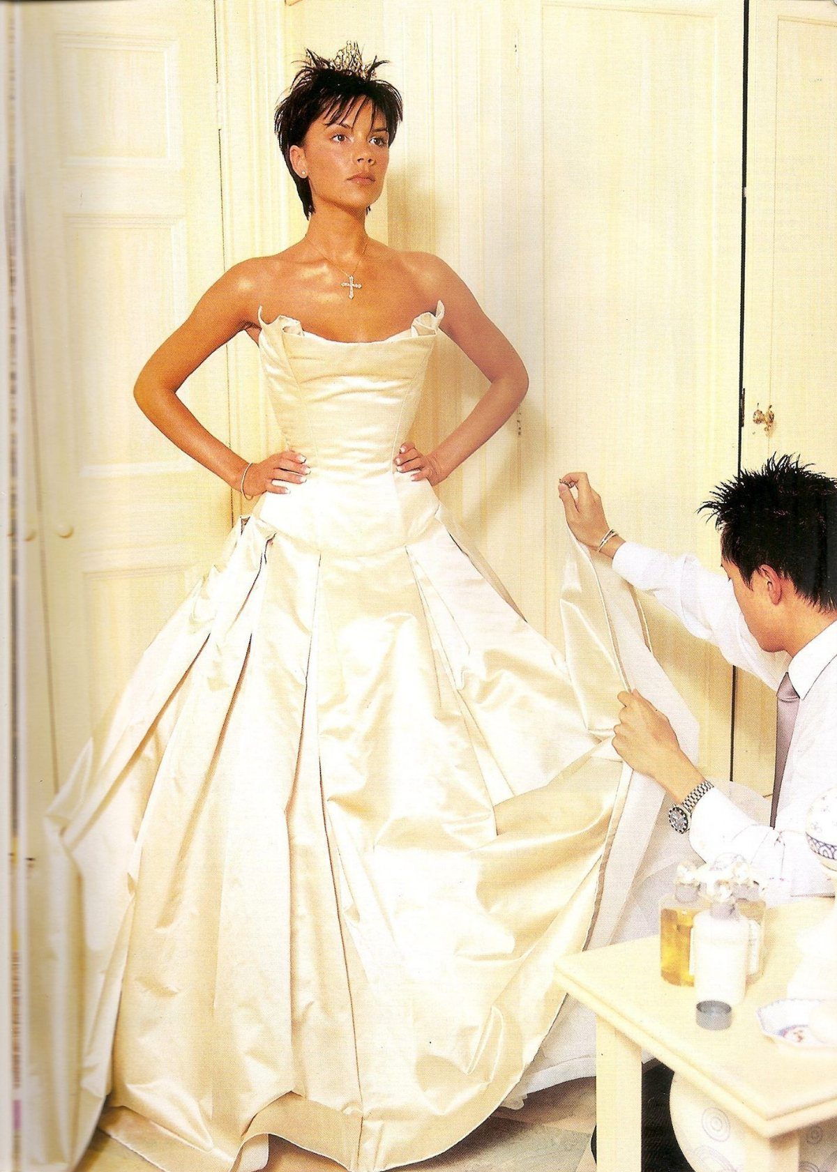 Iconic Wedding Dresses and 6 Stories They Still Tell 4 Woman posing in a voluminous strapless white satin wedding dress while a man adjusts the skirt.