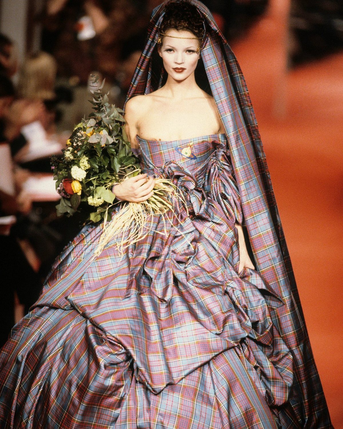 Iconic Wedding Dresses and 6 Stories They Still Tell 5 Model walking a runway in a voluminous, strapless plaid Vivienne Westwood wedding dress with heavy draping.