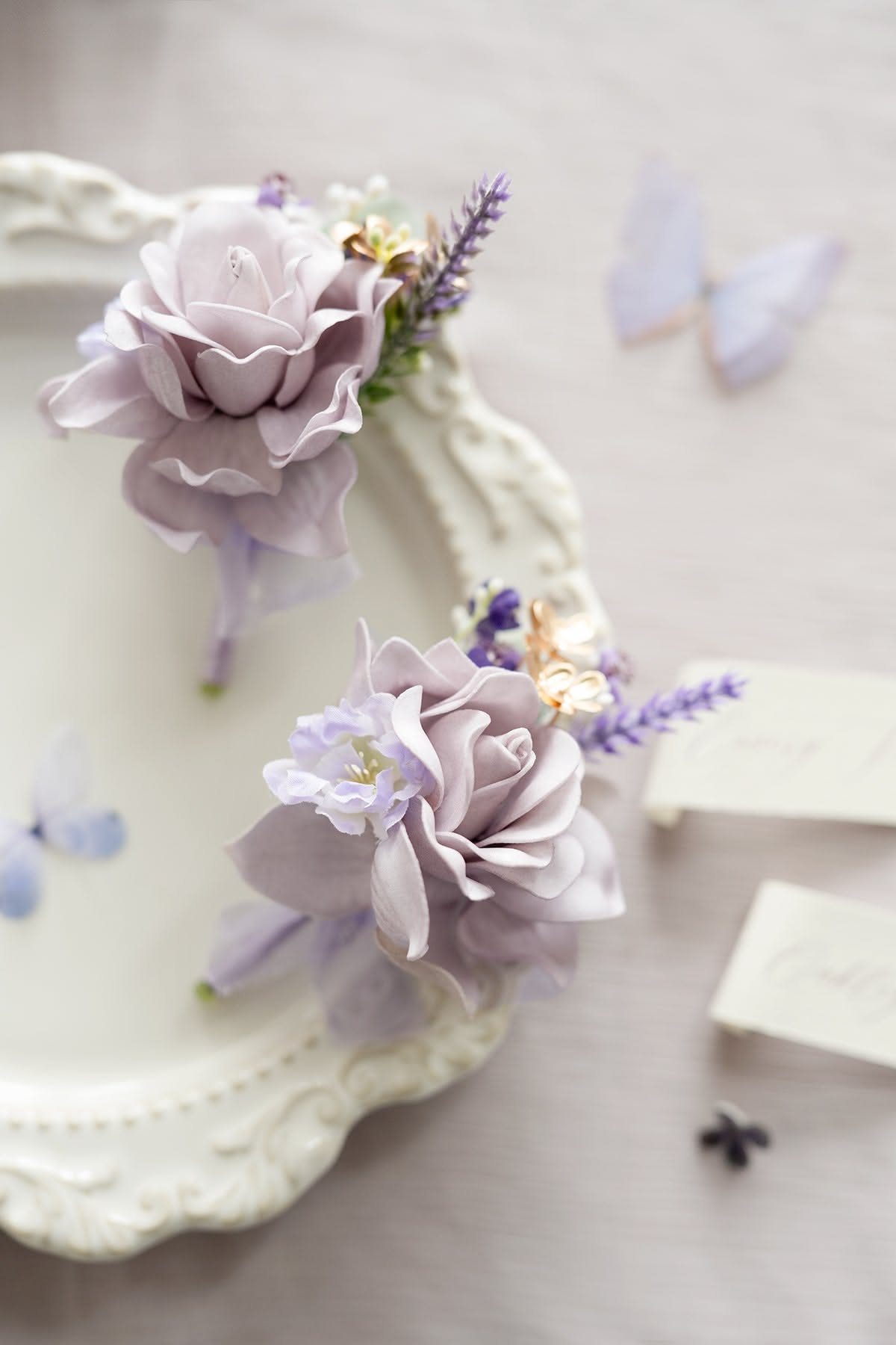 Two lavender floral boutonnieres with roses and lavender sprigs resting on a white decorative plate.