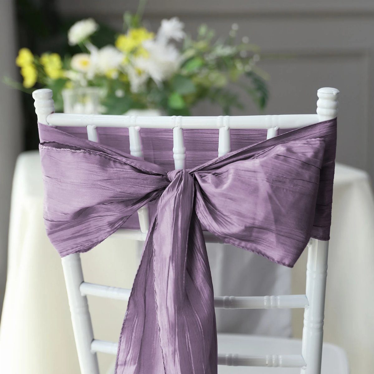 A white wooden chair decorated with a large lavender crinkle taffeta bow sash.