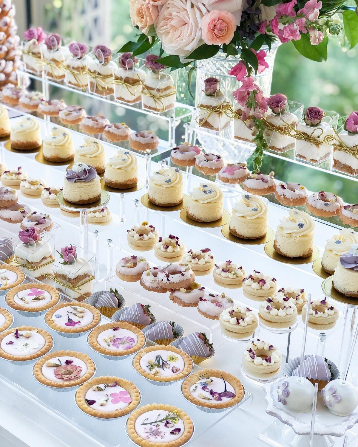 Assorted miniature desserts decorated with edible purple flowers and lavender sprigs on clear tiered stands.