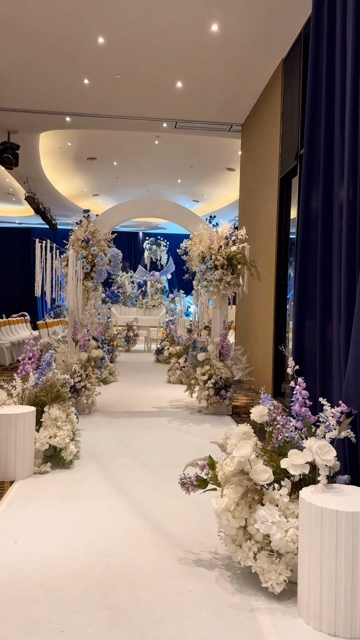White wedding aisle lined with lavender and white flowers against navy blue curtains.