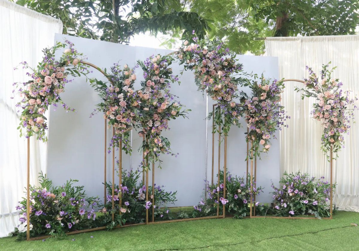 Gold floral arches with lavender and pink flowers set against a white backdrop on grass.