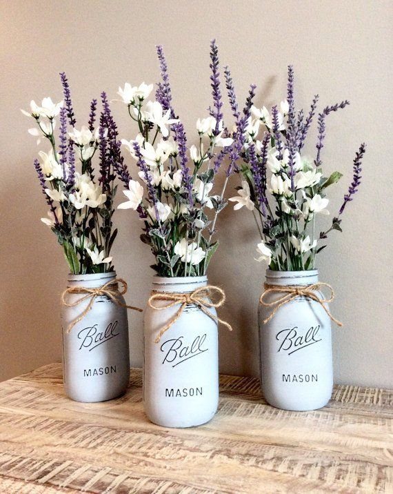 Three white mason jars with lavender and white flowers sitting on a wooden table.