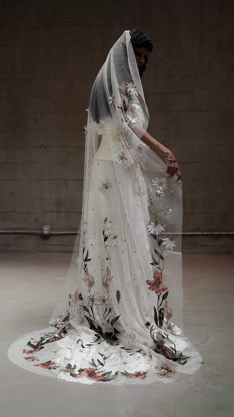 A person wearing a long, sheer white wedding veil decorated with large floral embroidery.
