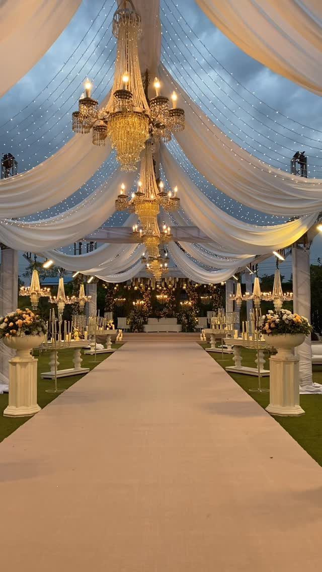 Mansion Wedding Venue Ideas: 17 Estate Settings for 2026 16 A decorated wedding aisle with white draping, crystal chandeliers, and a long beige runner under twilight skies.
