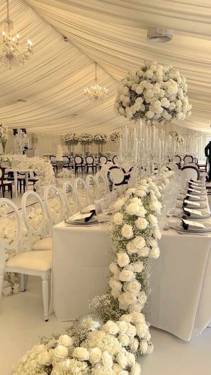 Mansion Wedding Venue Ideas: 17 Estate Settings for 2026 7 White rose garlands and crystal centerpieces decorate a formal wedding reception table under draped fabric ceilings.