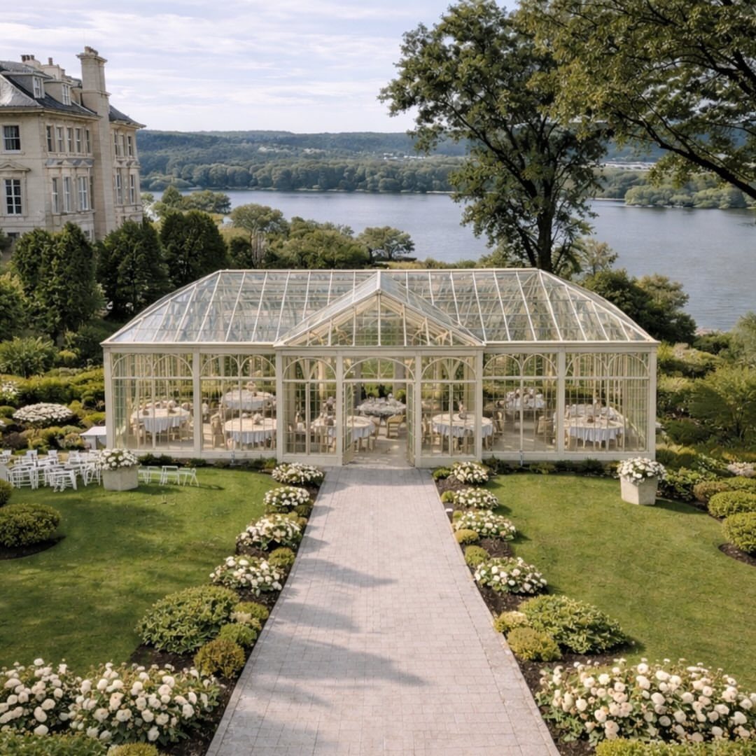 Mansion Wedding Venue Ideas: 17 Estate Settings for 2026 6 A white glass conservatory filled with dining tables situated in a lush garden by a river.