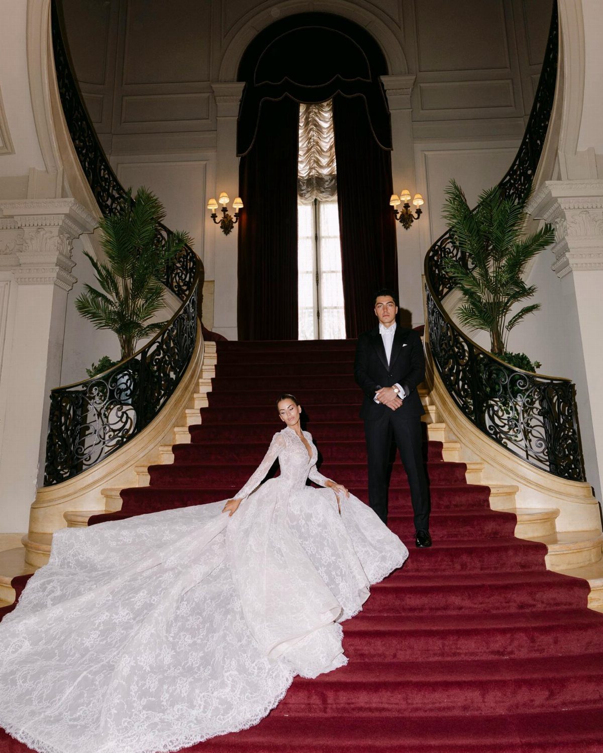 Mansion Wedding Venue Ideas: 17 Estate Settings for 2026 3 A bride and groom posing on a grand red staircase inside a luxurious mansion.