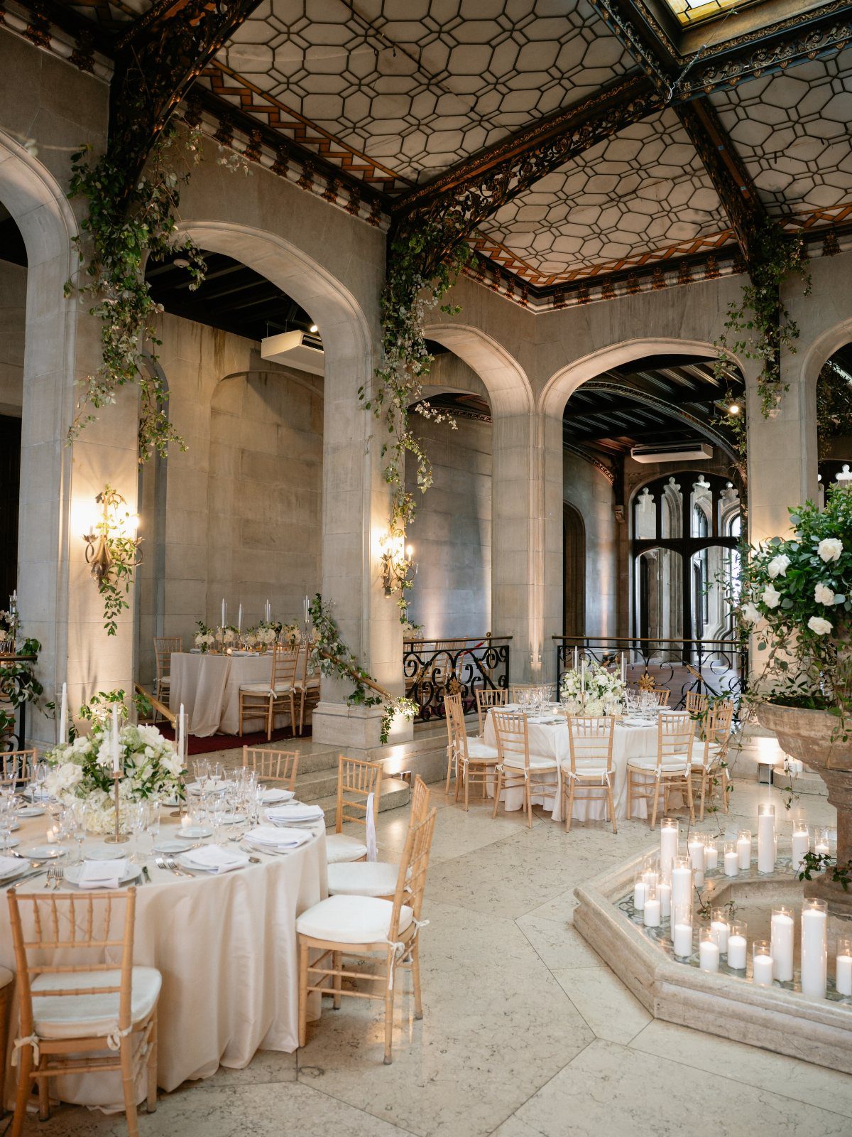 Mansion Wedding Venue Ideas: 17 Estate Settings for 2026 1 Elegant wedding reception tables set inside a grand stone hall with arched ceilings and greenery.