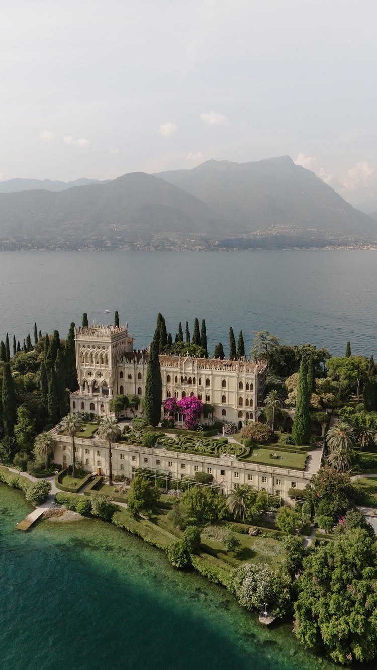 Mansion Wedding Venue Ideas: 17 Estate Settings for 2026 11 A large historic stone mansion situated on a green peninsula overlooking a vast lake and mountains.