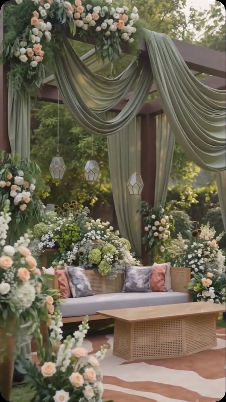 Mansion Wedding Venue Ideas: 17 Estate Settings for 2026 10 Outdoor lounge area with floral arrangements, draped green fabric, and a sofa under a wooden pergola.