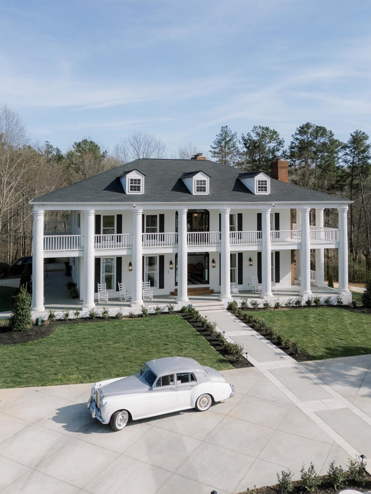Mansion Wedding Venue Ideas: 17 Estate Settings for 2026 17 A large white colonial mansion with tall columns and a vintage white car in the driveway.