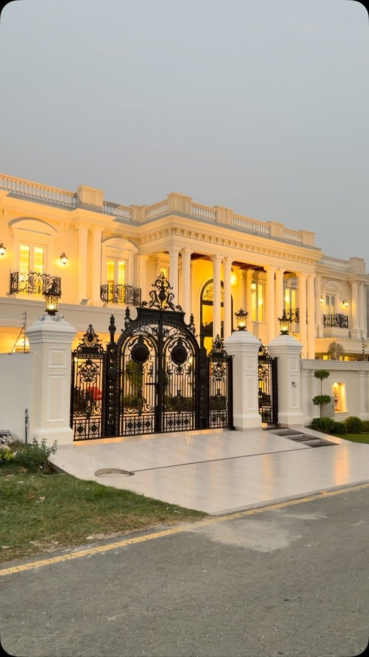 Mansion Wedding Venue Ideas: 17 Estate Settings for 2026 15 A grand white mansion with warm lighting behind large black wrought-iron gates.