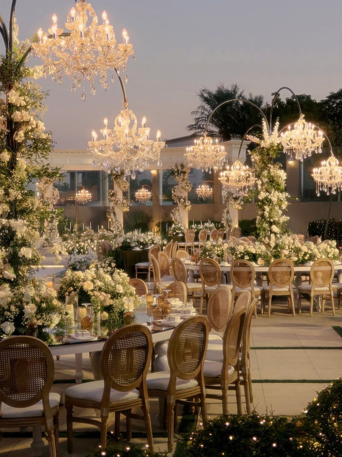 15 Most Beautiful Wedding Venues for 2026 8 Elegant outdoor wedding reception with white flowers, cane chairs, and hanging crystal chandeliers.