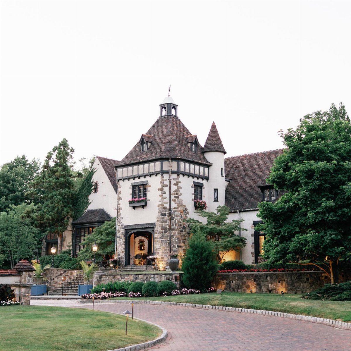 15 Most Beautiful Wedding Venues for 2026 4 A large stone mansion with a turret and tiled roof surrounded by green trees and landscaping.
