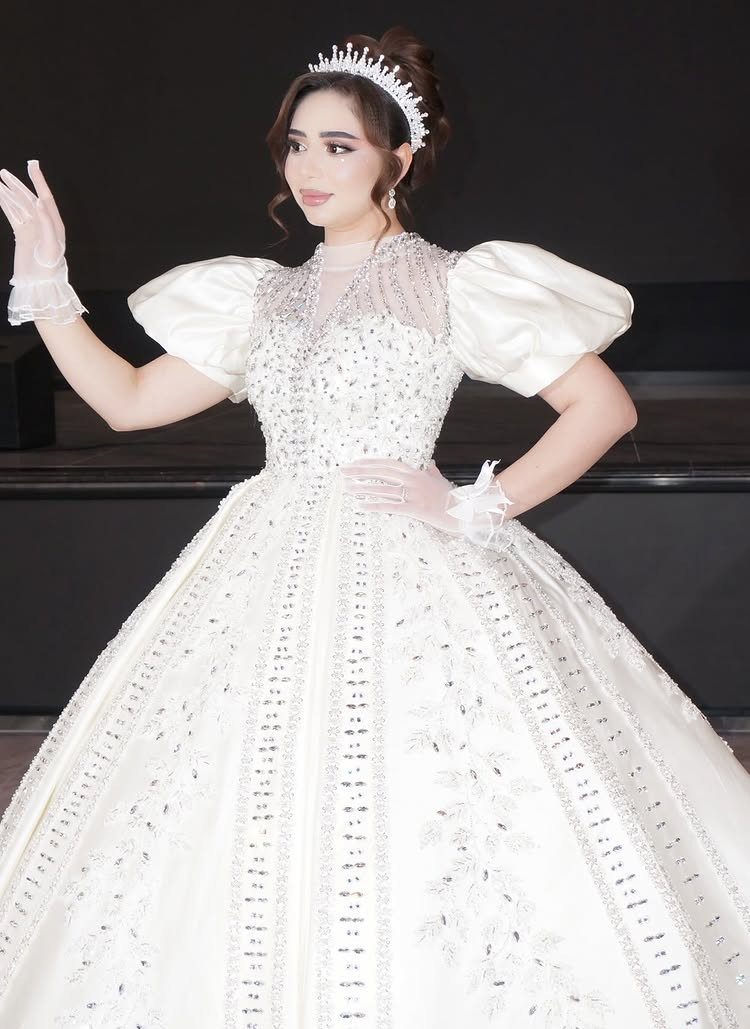 Woman in a voluminous white ball gown with silver embellishments and a sparkling tiara.