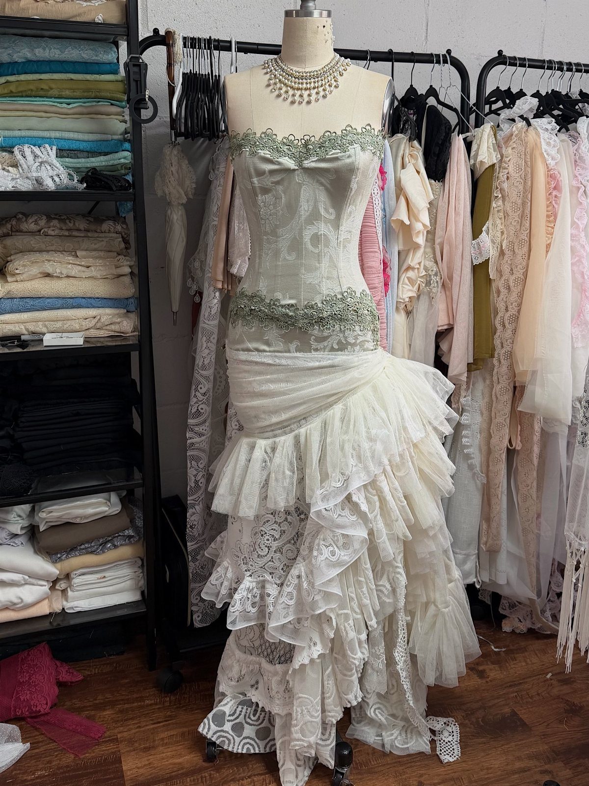 A cream lace mermaid wedding dress with ruffled tiers displayed on a mannequin in a studio.