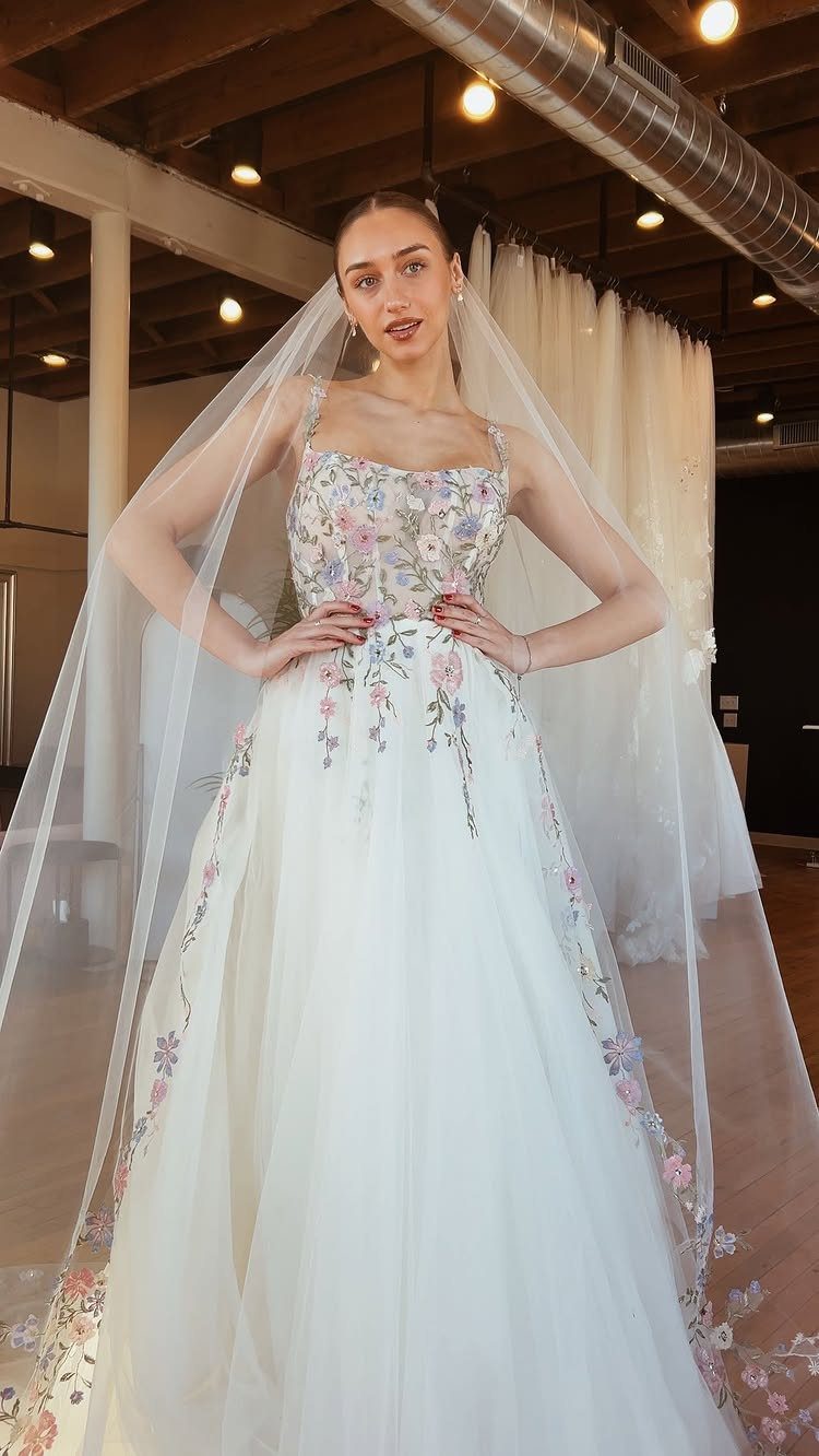 A woman wearing a white floral embroidered wedding dress and a long sheer veil.
