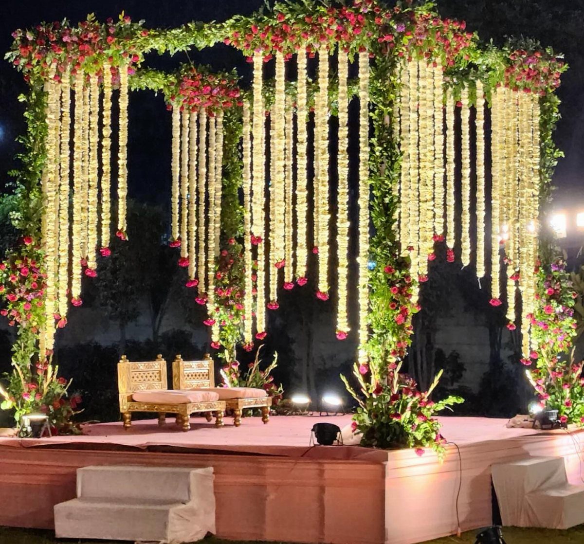 Floral archway with hanging white flower strands and red roses over gold wedding chairs.