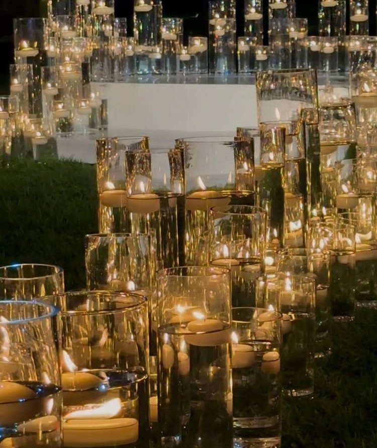 Floating white candles in clear glass cylinders creating a glowing pathway at night.
