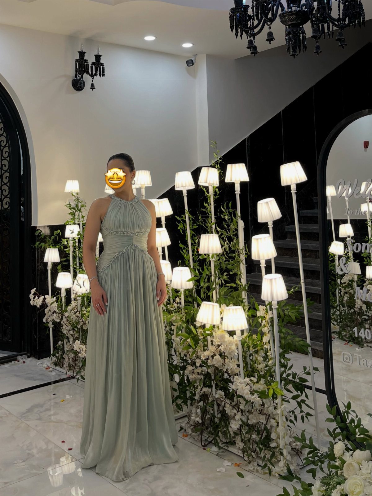 A woman posing in a long, sleeveless, mint green pleated formal gown indoors.