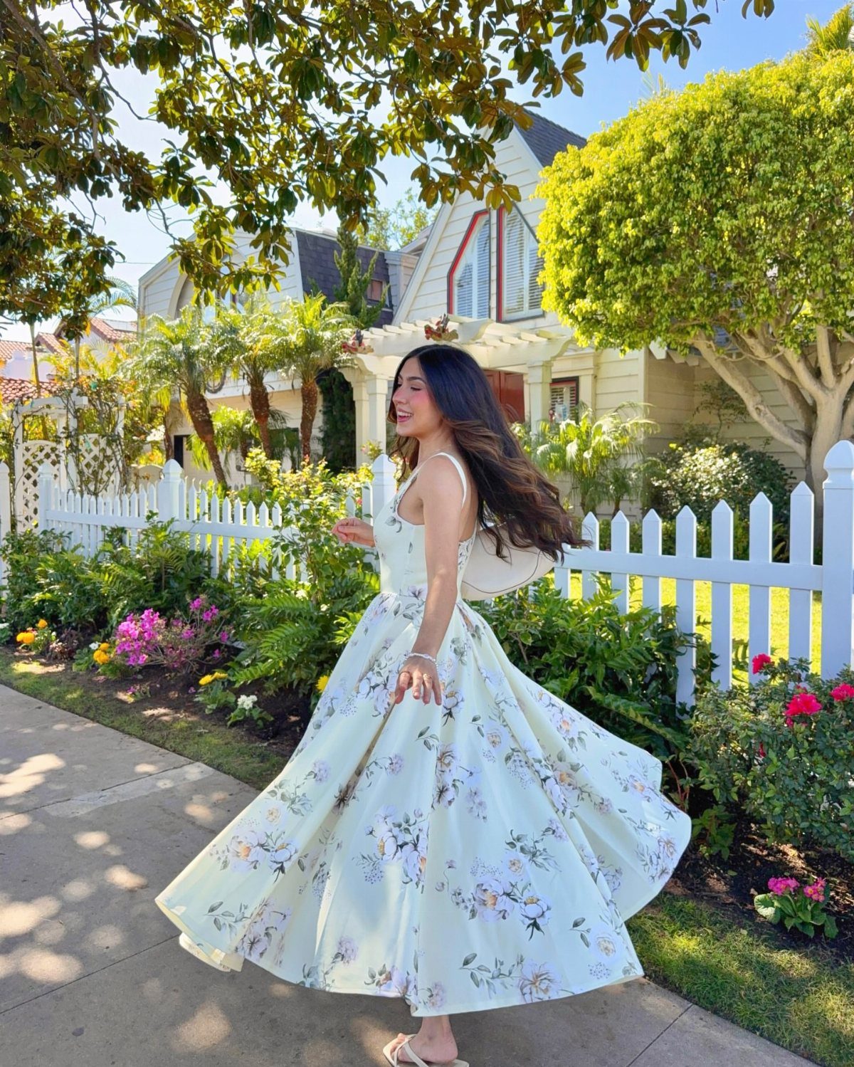 A woman twirling in a light yellow midi dress with a pastel floral pattern outdoors.