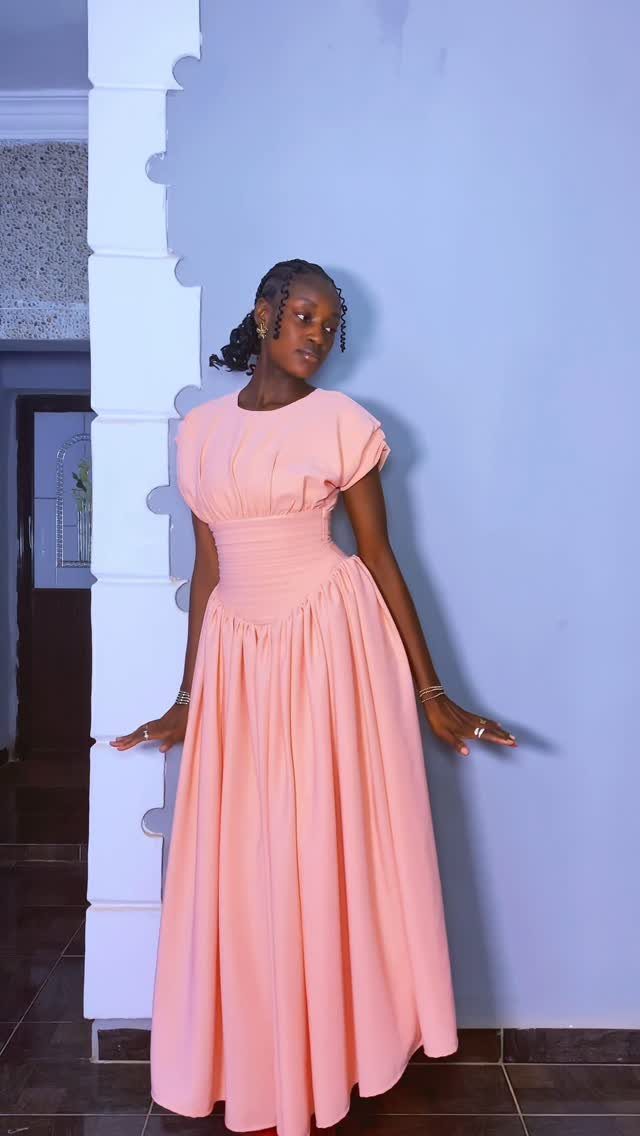 A woman in a peach-colored midi dress posing against a light blue wall.