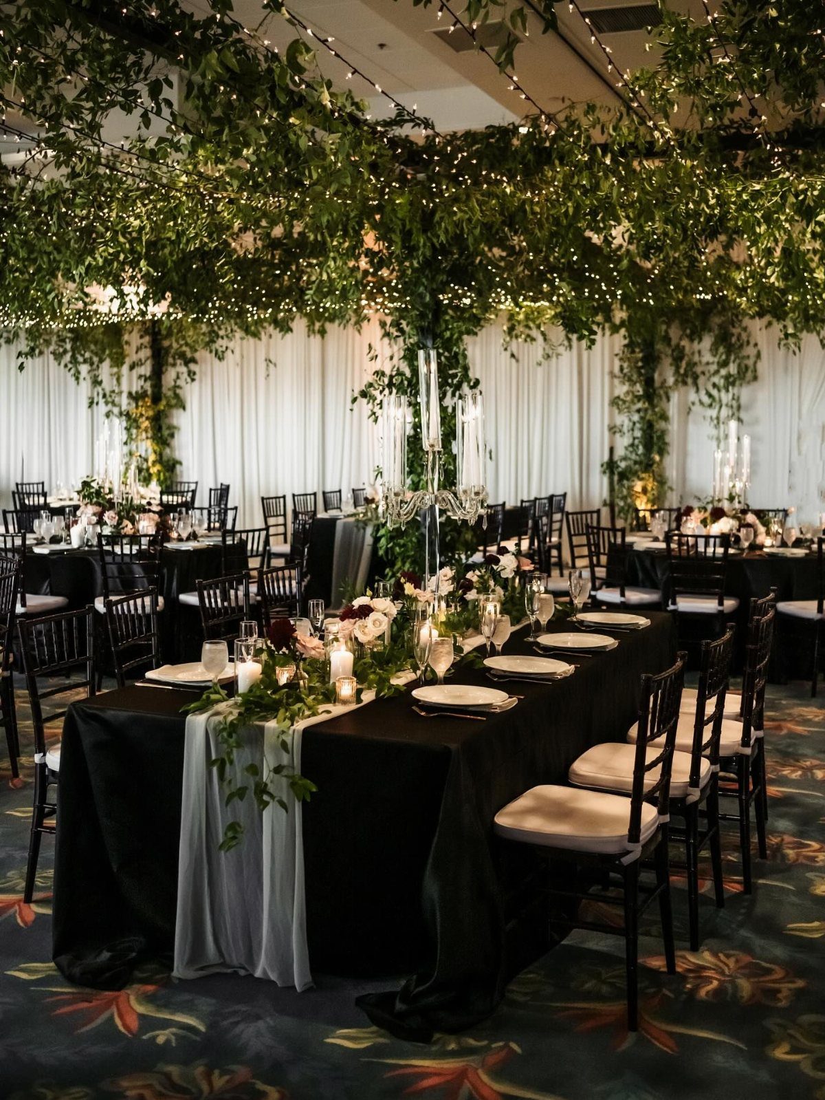 Purple and Black Wedding Theme: 8 Ideas That Actually Work 4 A long banquet table with black linens, white floral arrangements, and greenery under fairy lights.