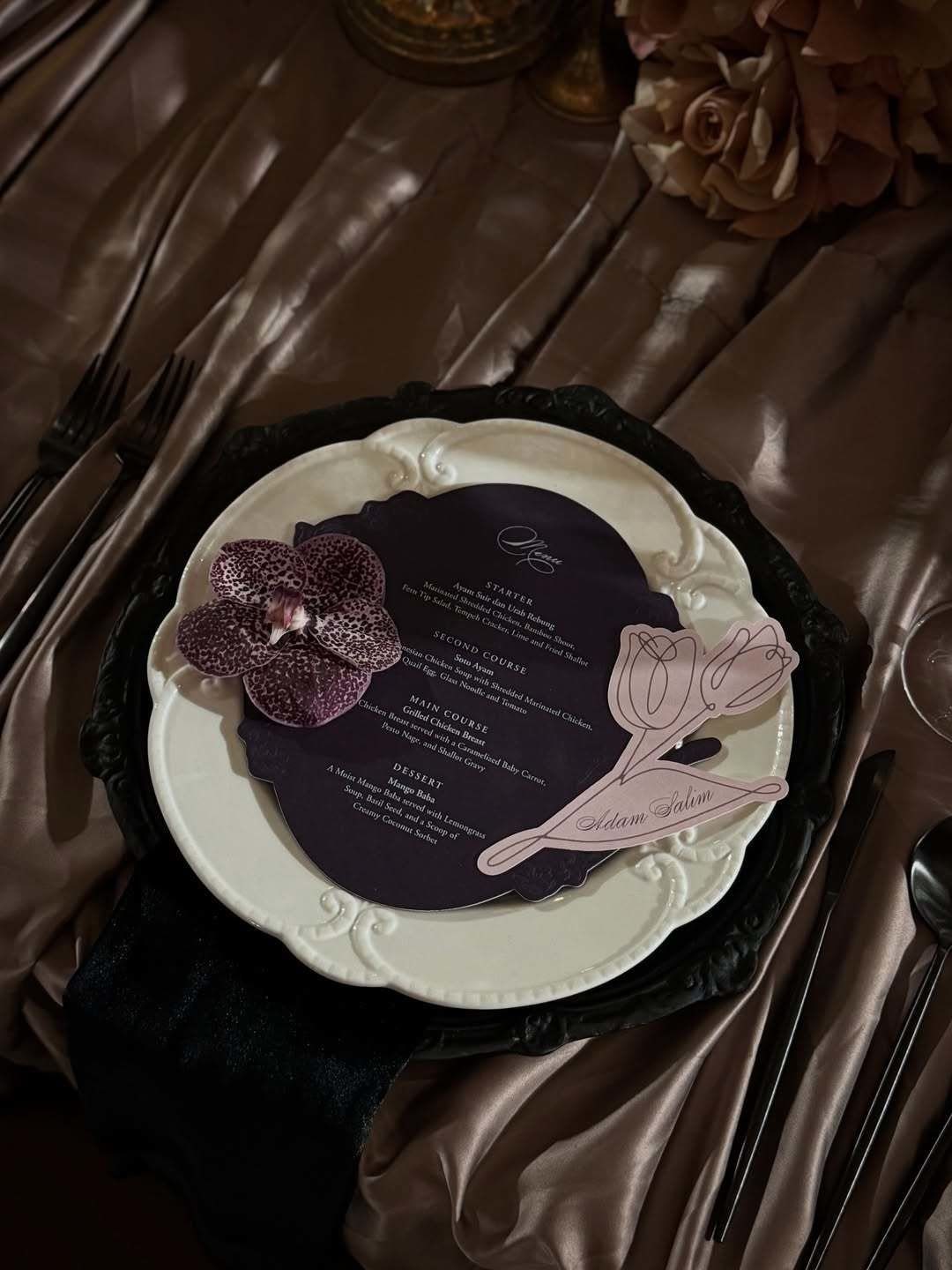 Purple and Black Wedding Theme: 8 Ideas That Actually Work 7 A dark purple menu card with pink floral designs sits on a white plate.