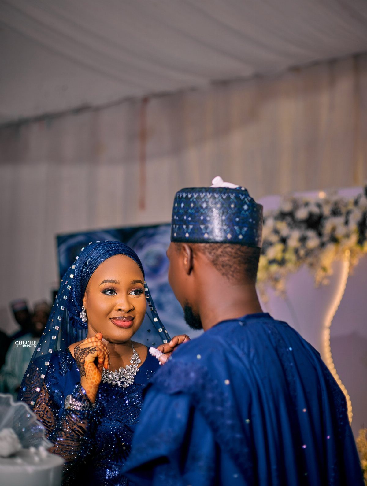 A smiling woman in royal blue lace attire looking at a man in matching blue traditional clothing.